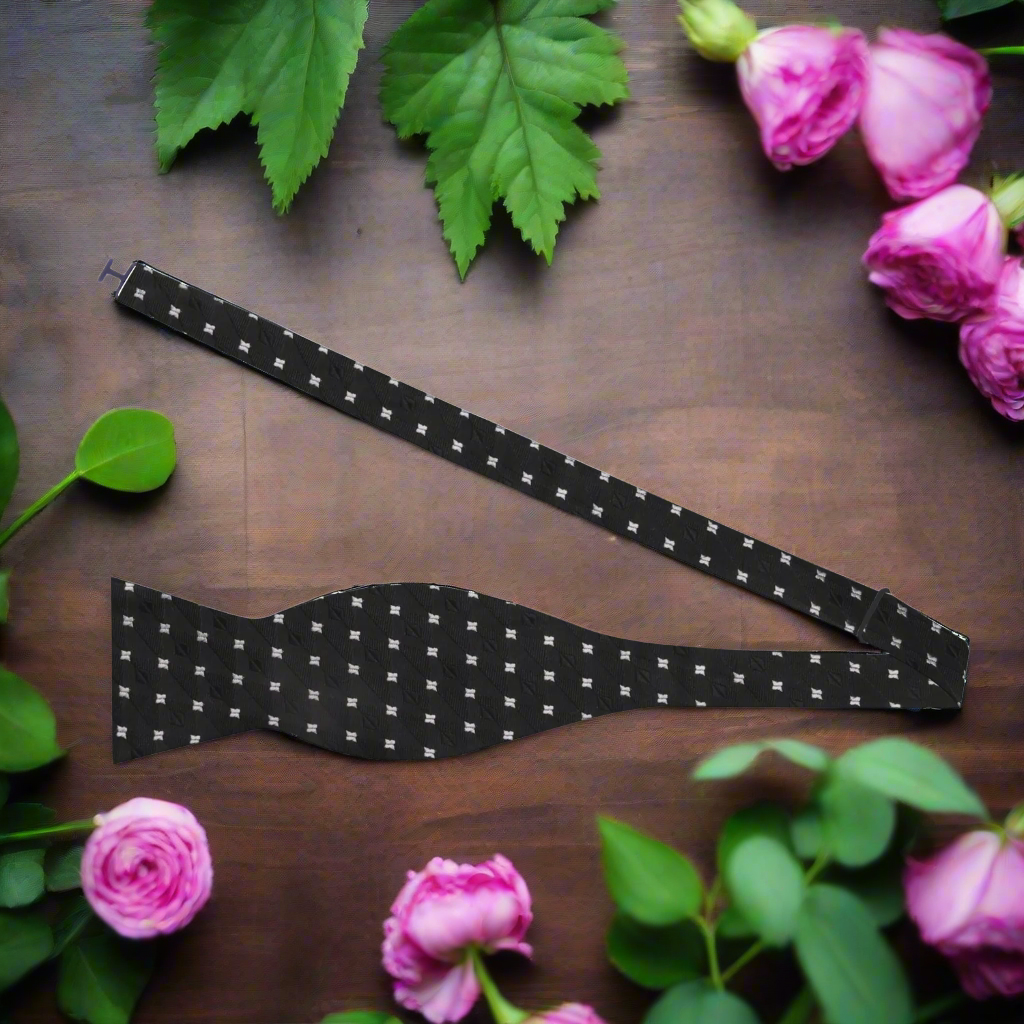 Elegant black self-tie bow tie with light grey geometric diamond check pattern, displayed on a formal shirt.