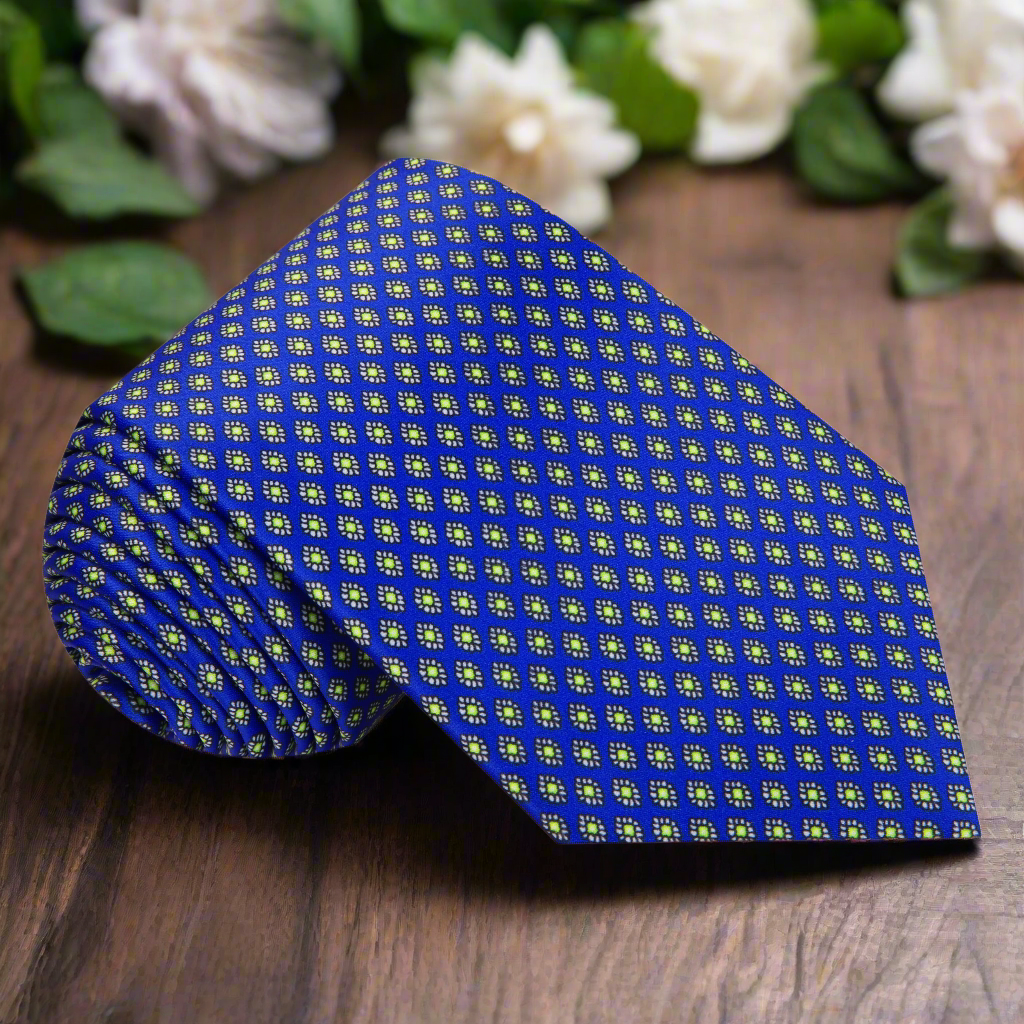 Top-down view of blue silk necktie with green medallion pattern on a white shirt.