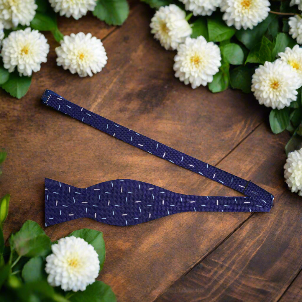 Matching navy blue pocket square featuring bold stripes, complemented by the bow tie.