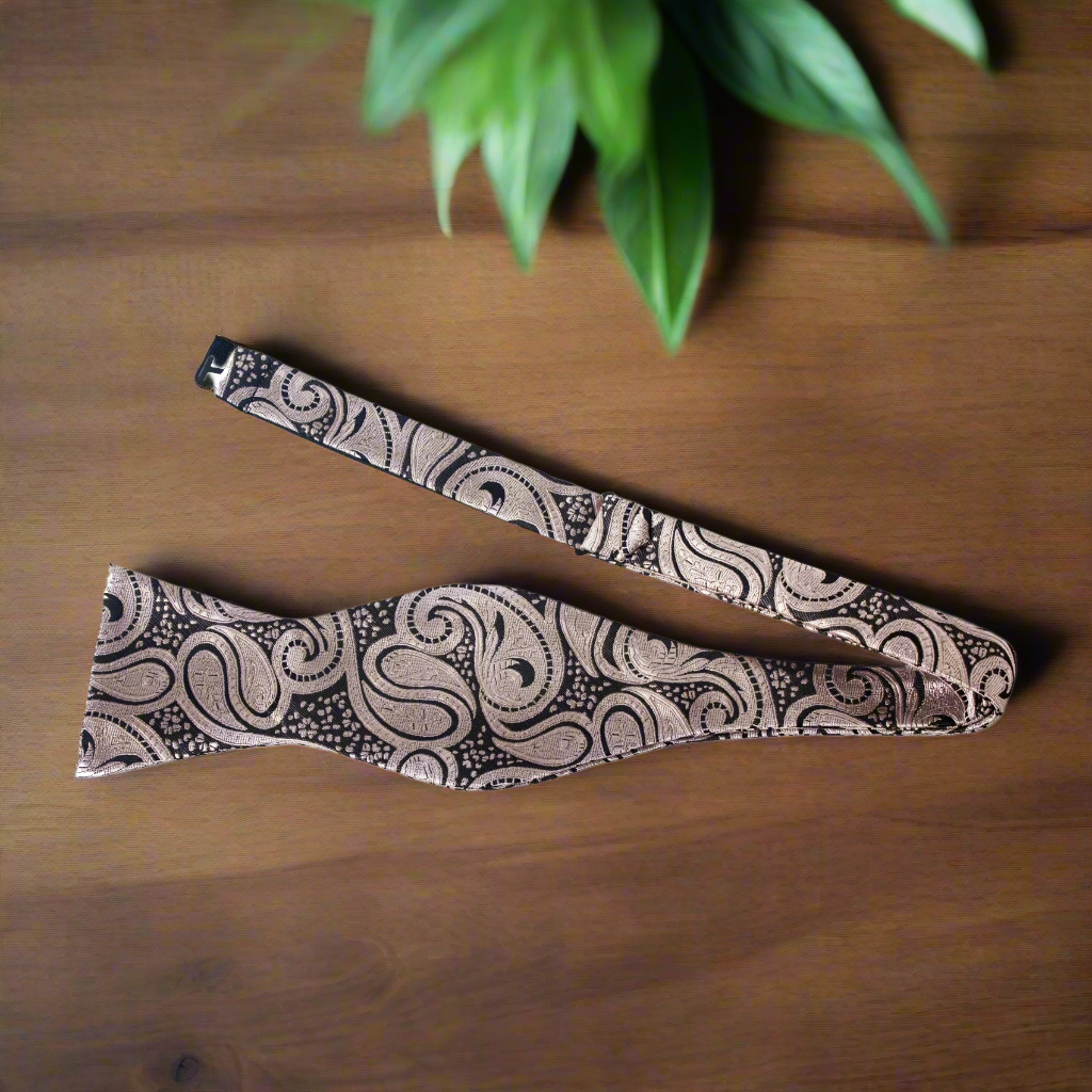 Elegant black and blue paisley self-tie bow tie displayed on a crisp white shirt.