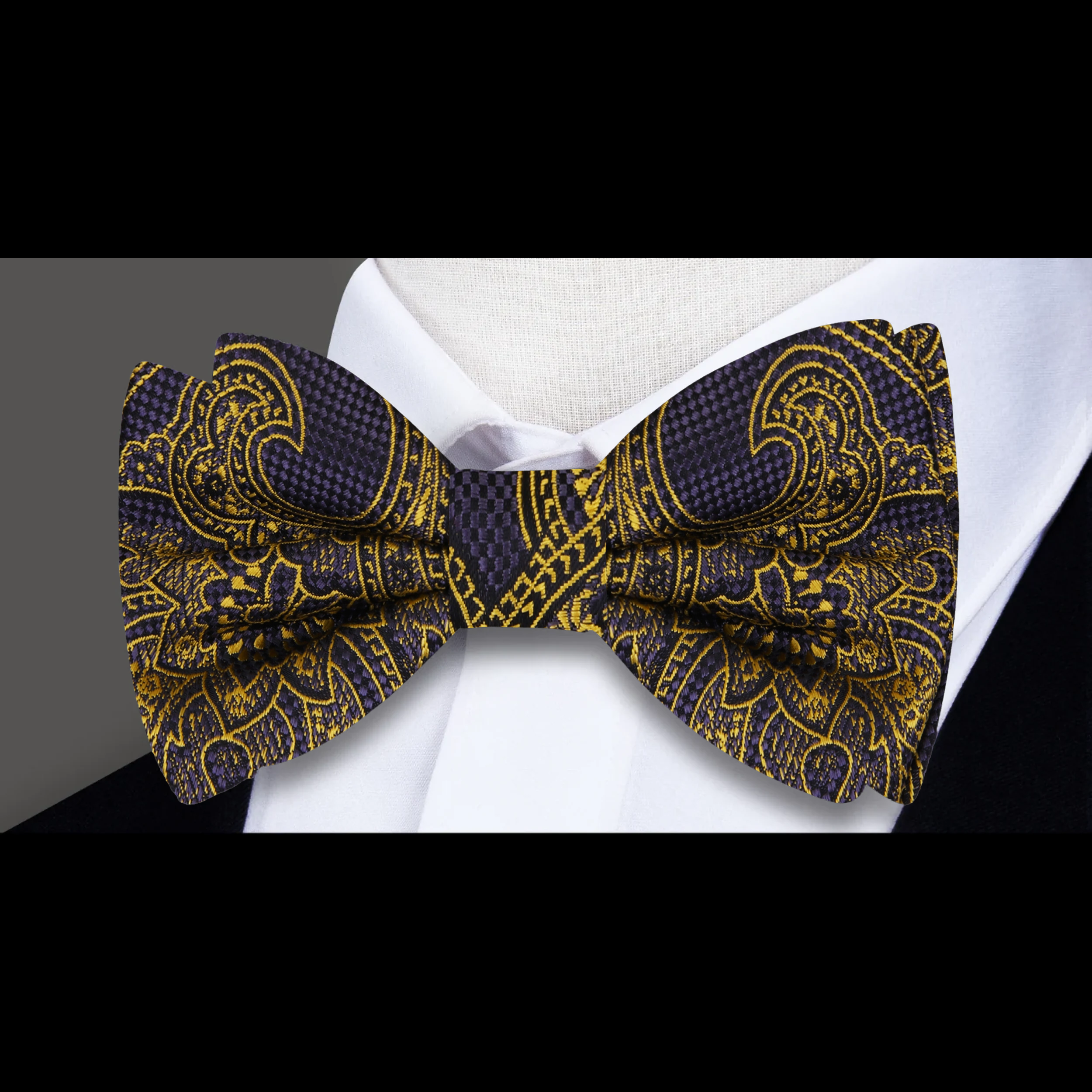 Elegant black and gold paisley bow tie displayed on a crisp white shirt, perfect for formal occasions.