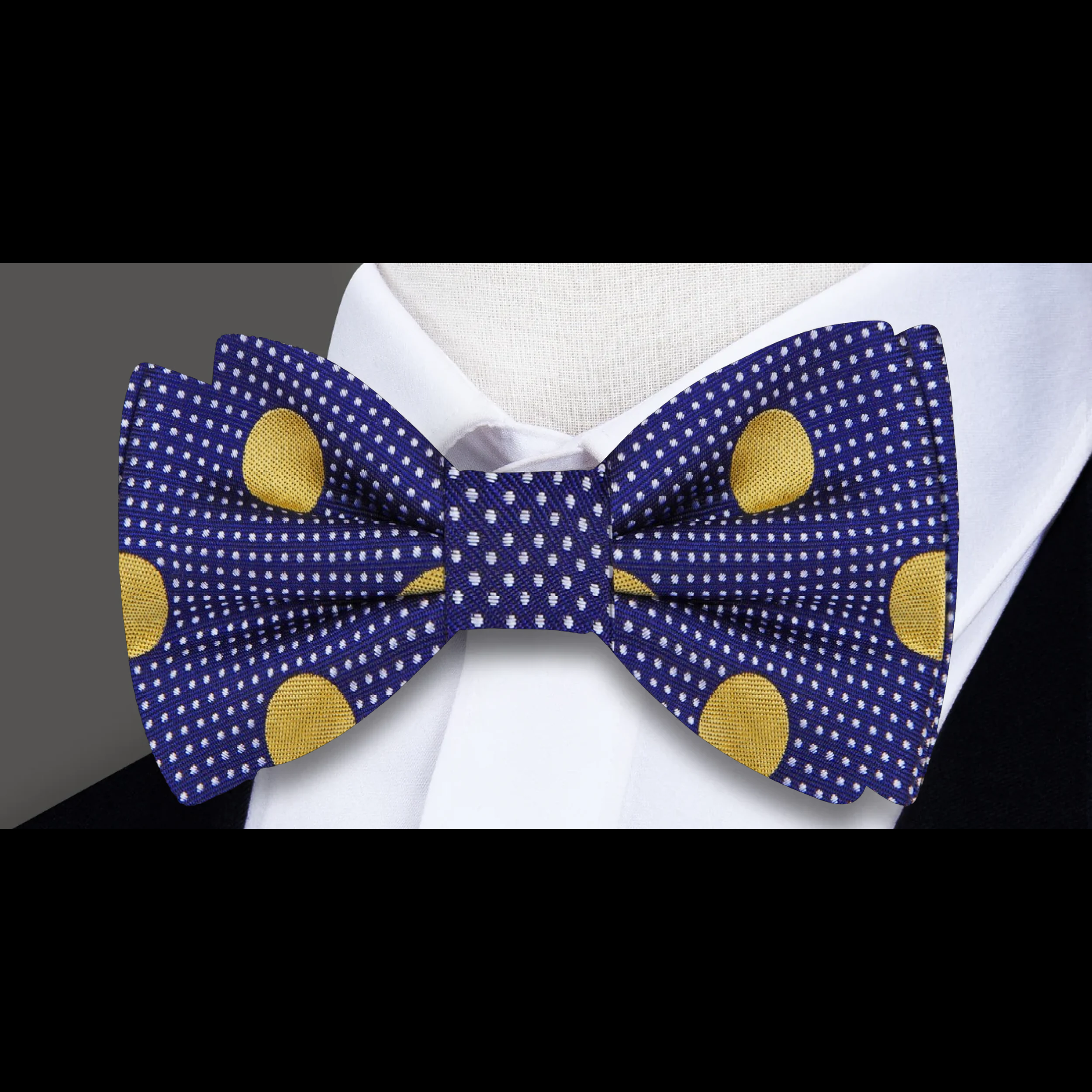 Elegant dark blue bow tie with gold polka dots displayed on a light grey dress shirt.
