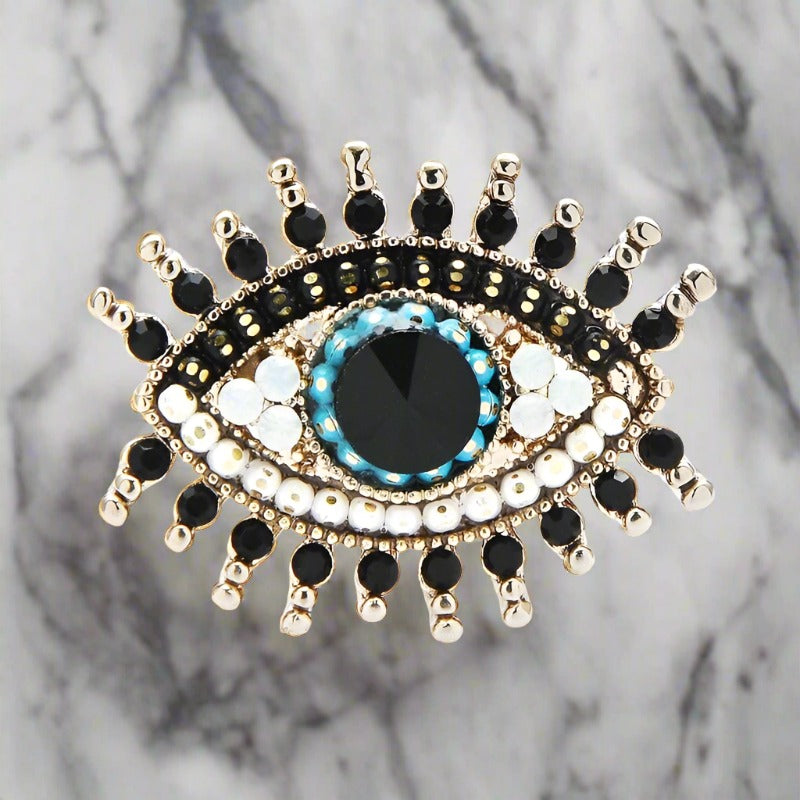 Close-up of the mystical eye lapel pin featuring clear stones on a tailored suit.