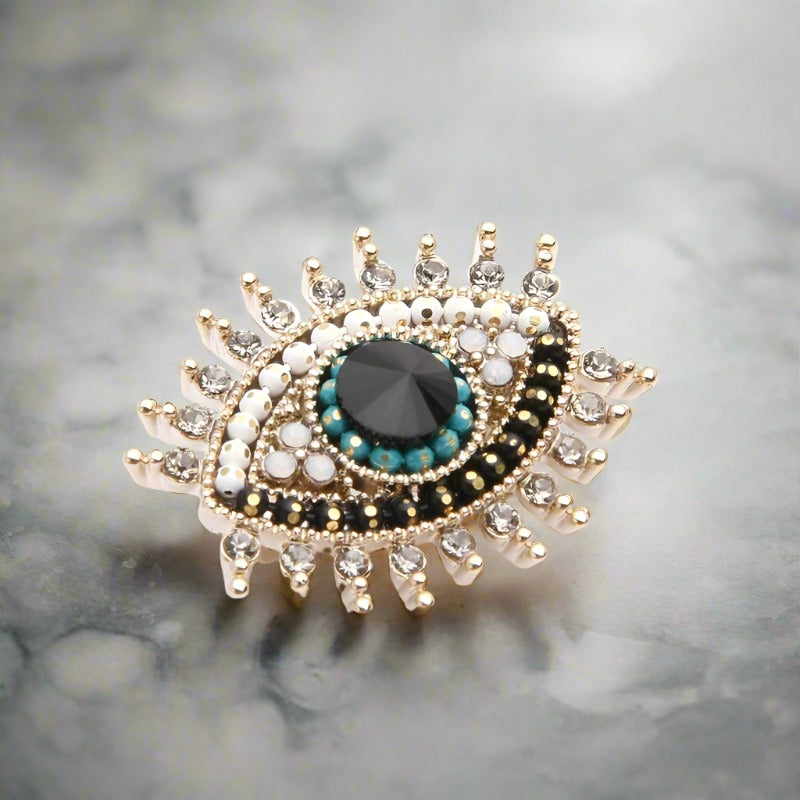 Close-up of the mystical eye lapel pin featuring clear stones on a tailored suit.