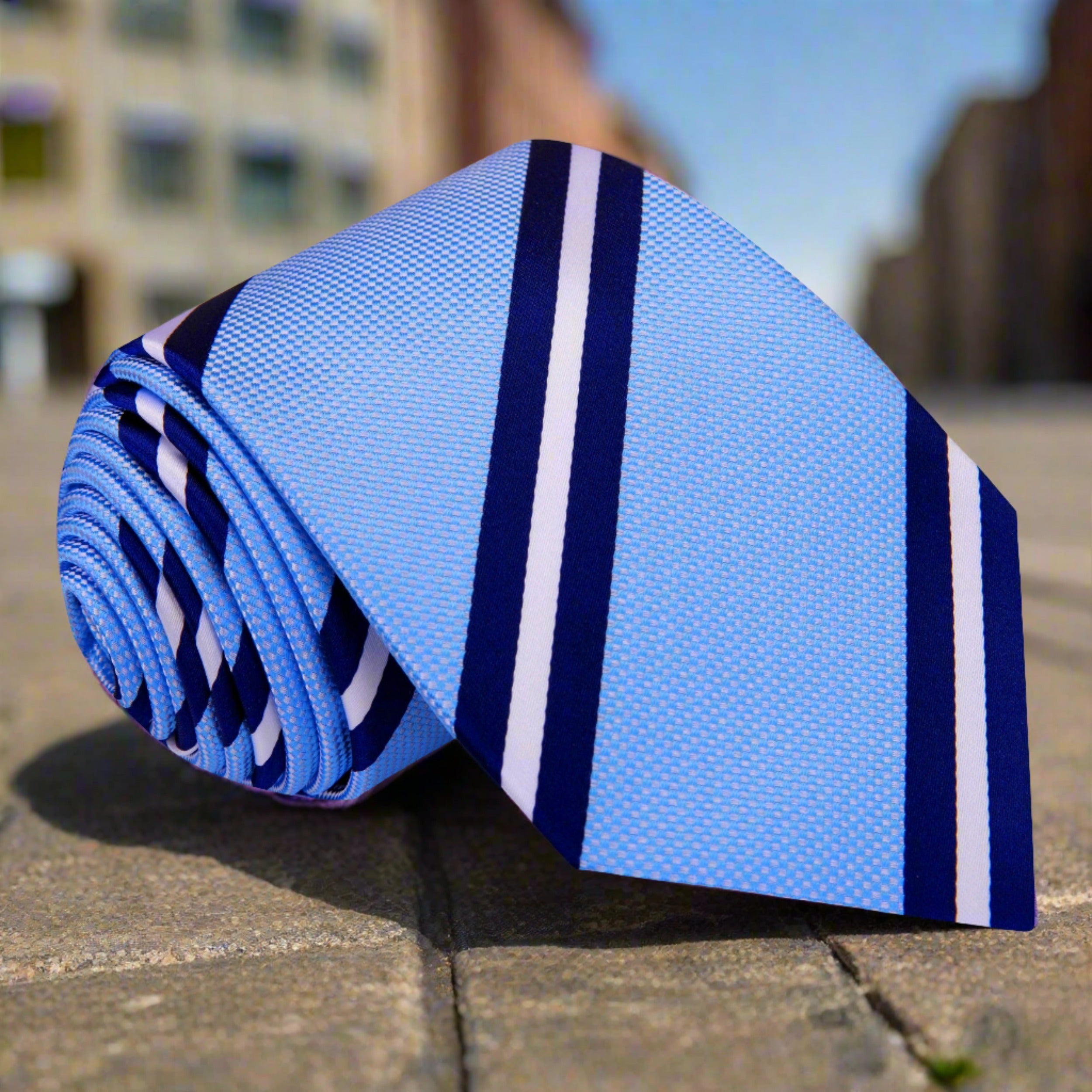 Elegant striped silk necktie in light blue with dark blue and white stripes, perfect for formal wear.