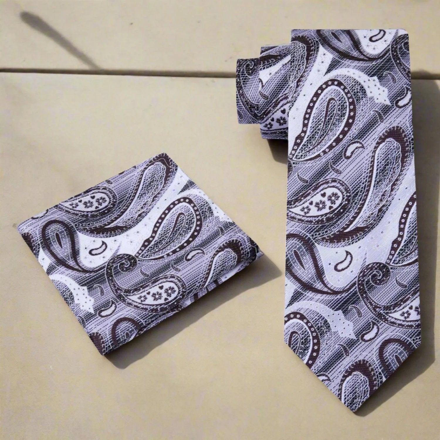 Close-up of the intricate paisley design on a light grey and brown silk tie, showcasing its craftsmanship.