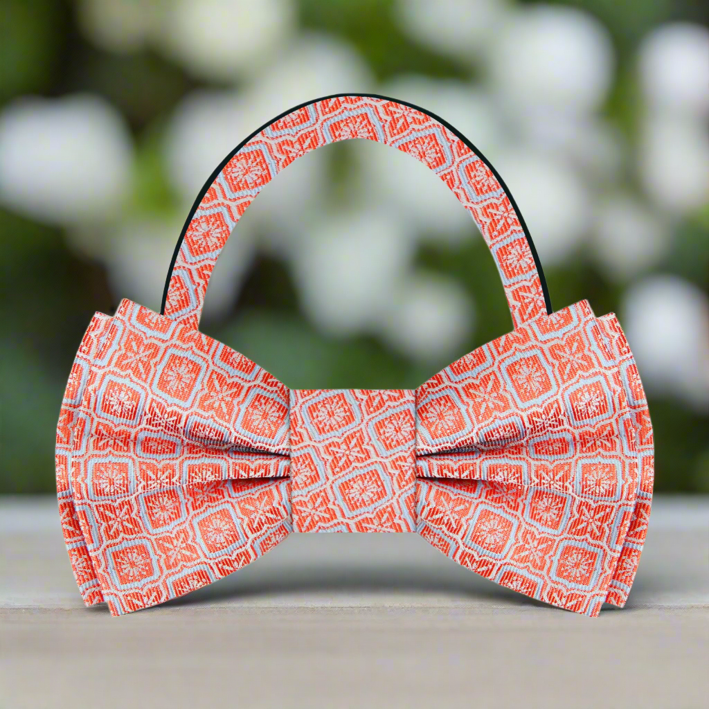 Flat lay of the vibrant geometric silk bow tie alongside a charcoal grey suit and a pocket square.