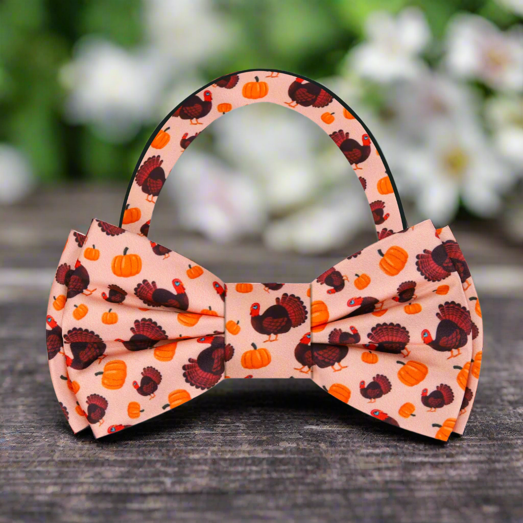 Front view of festive fall bow tie with turkeys and pumpkins in orange and brown tones, styled on white shirt.