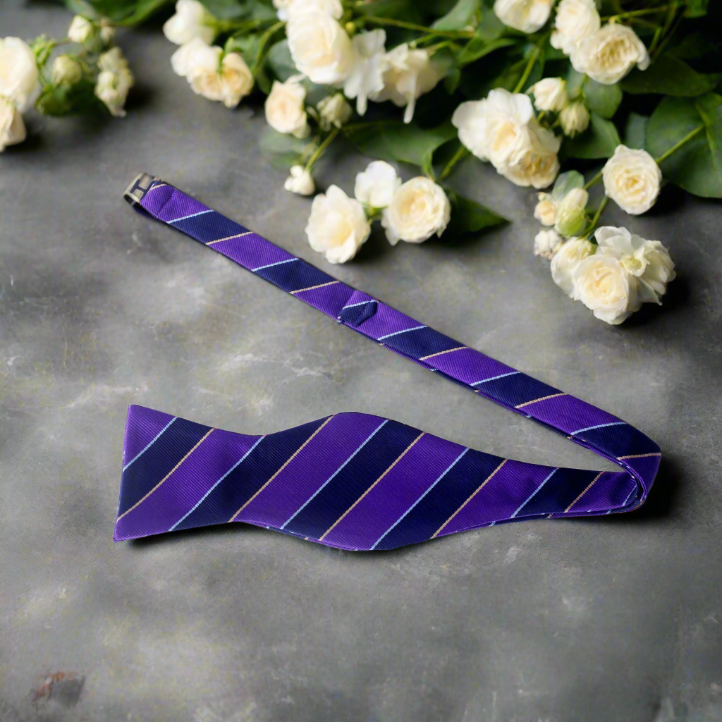 Close-up of dark blue and purple silk self-tie bow tie with stripe pattern