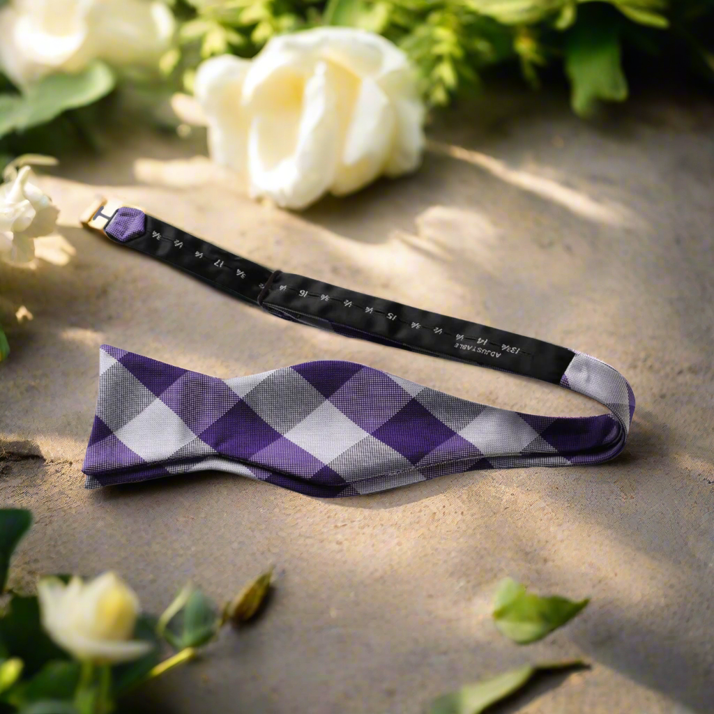Man adjusting a vibrant plaid self-tie bow tie with a classic suit for a formal event