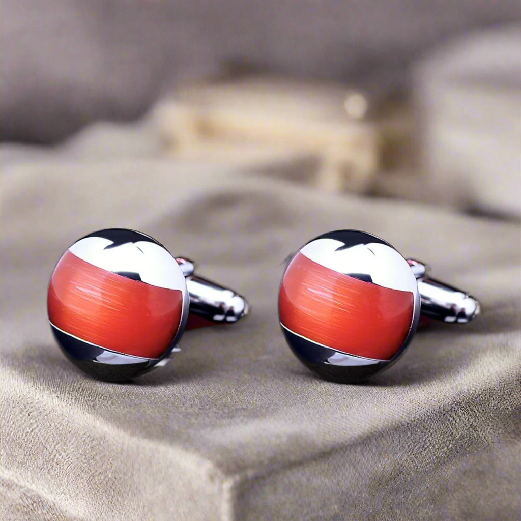 Close-up view of chrome cufflinks with red accents against a charcoal suit.