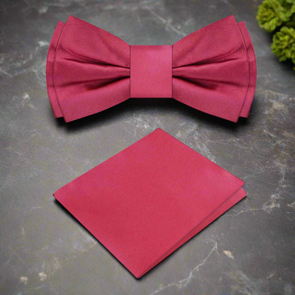 The deep red silk bow tie displayed alongside a navy suit, highlighting its sophisticated color contrast.