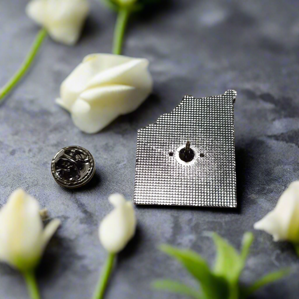 The lapel pin set beside a crisp white dress shirt on a wooden table.