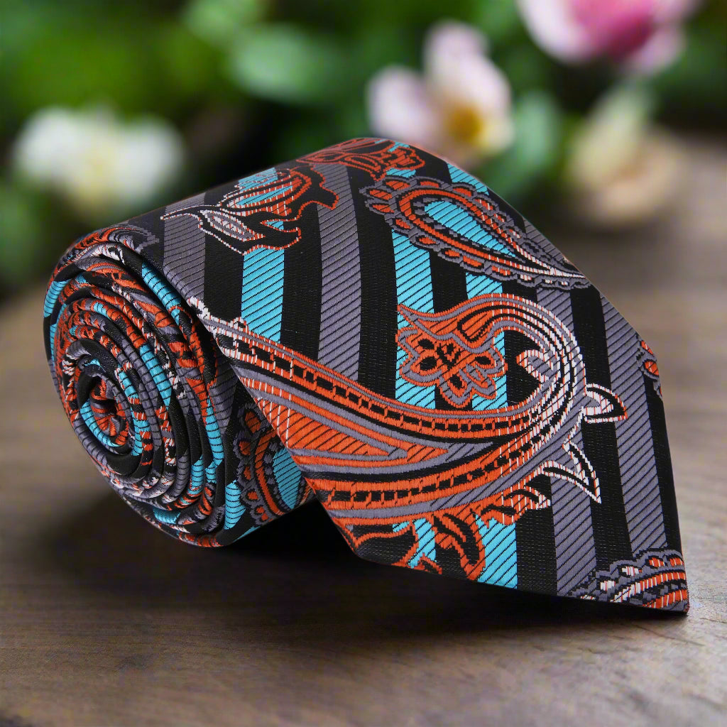 A close-up of the silk tie’s paisley and stripe pattern in black, blue, and copper tones on a white shirt