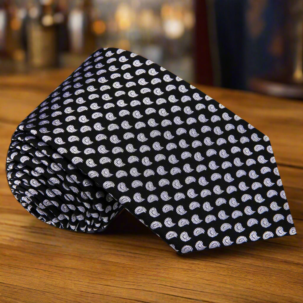 Black paisley necktie displayed on a light grey suit, showcasing its elegant design.