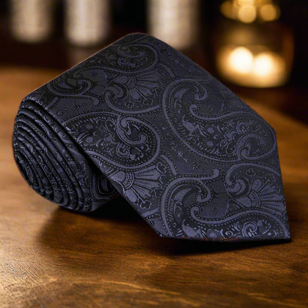 Elegant black paisley silk tie displayed on a white dress shirt, showcasing its intricate design.