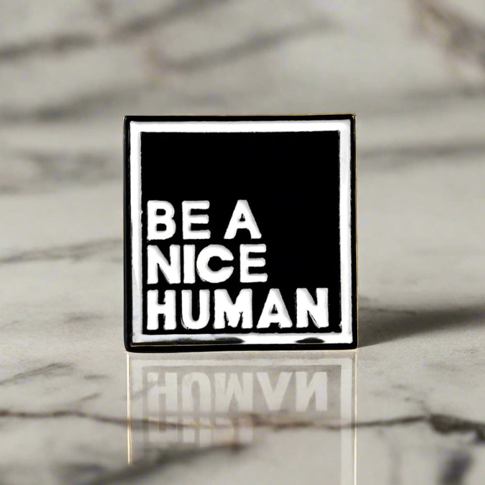 Close-up of motivational lapel pin on a white dress shirt showcasing the message Be A Nice Human