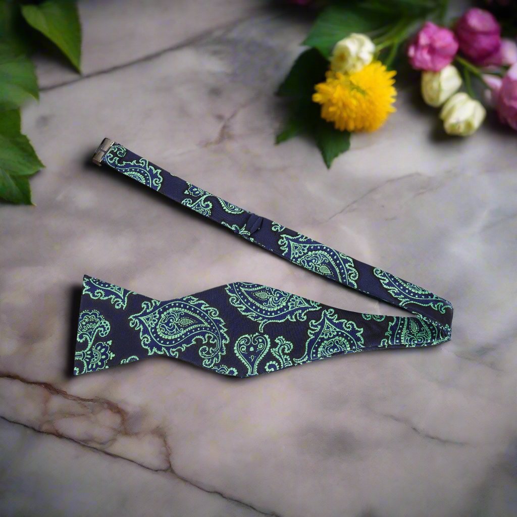 Elegant dark blue paisley self-tie bow tie displayed on a wooden table, showcasing its intricate design.
