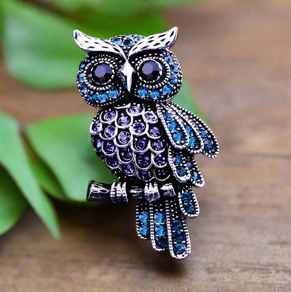 Front-facing owl lapel pin with brown speckles and miniature glasses, styled on a navy suit
