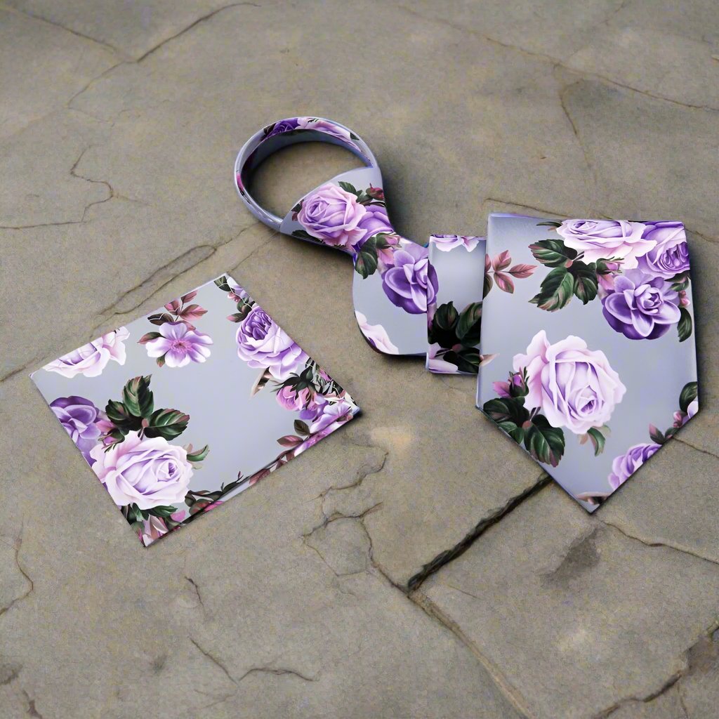 Elegant floral silk necktie displayed against a light grey suit, showcasing its intricate design of green leaves and pink roses.
