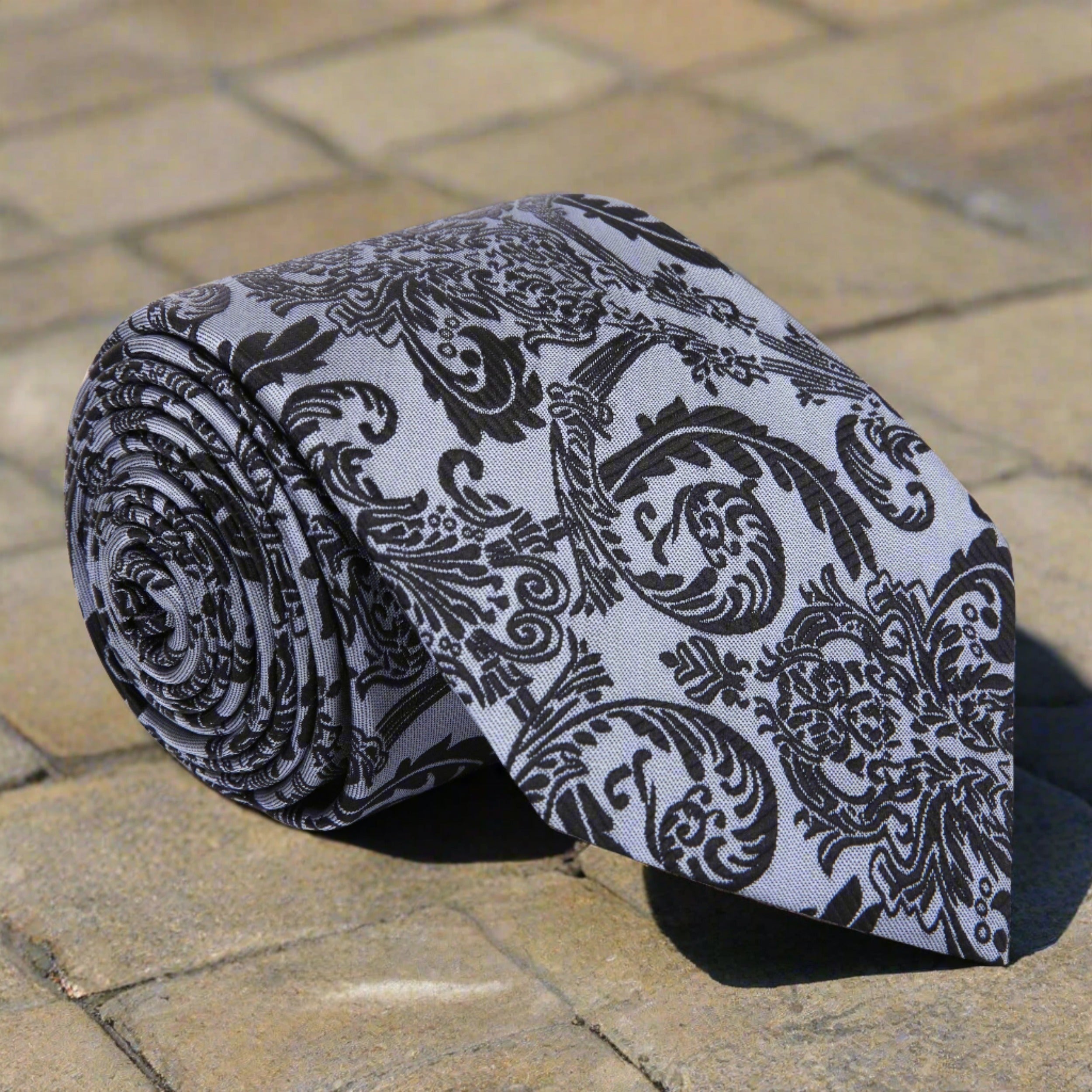 Elegant grey silk necktie with black floral pattern draped over a suit jacket