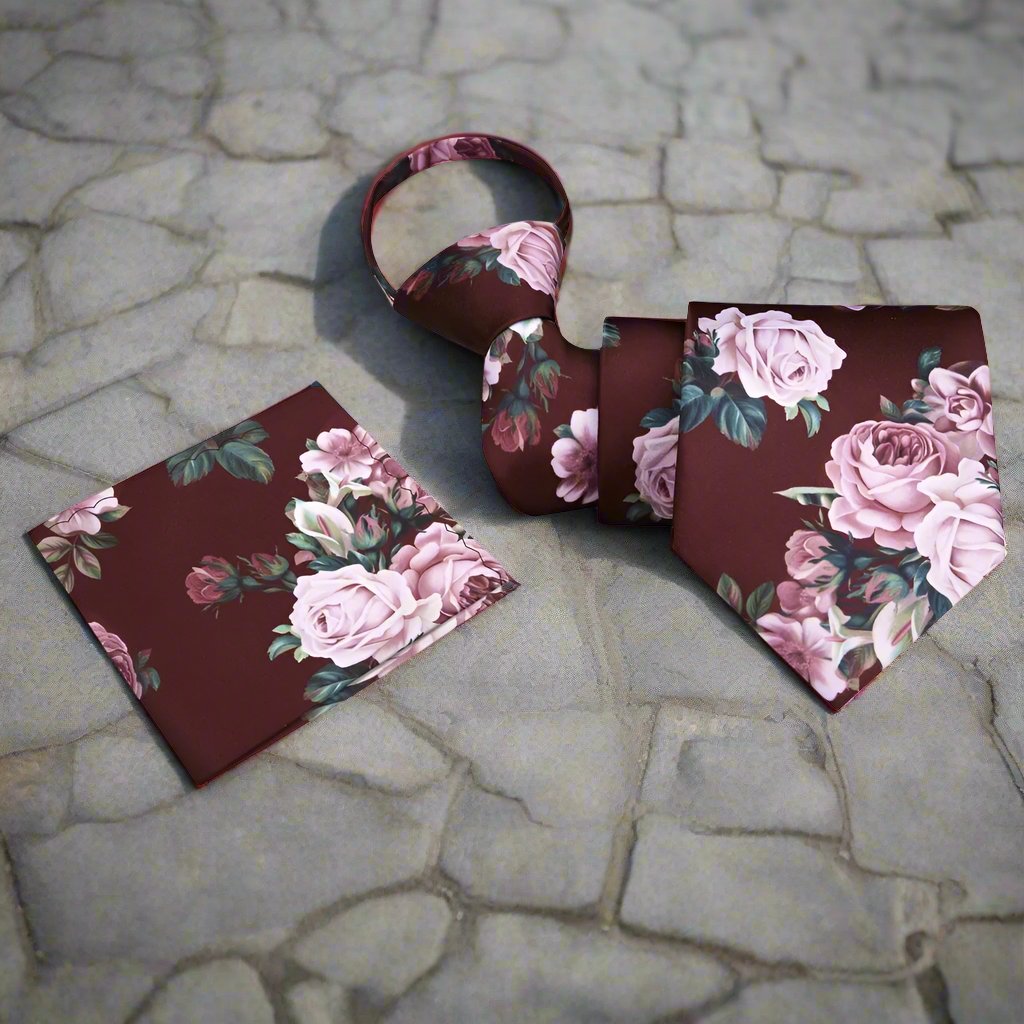 Elegant floral silk necktie displayed against a light grey suit, showcasing its intricate design of green leaves and pink roses.