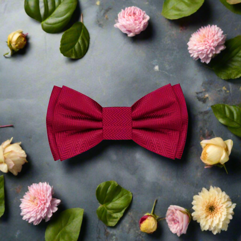 Stylish garnet red silk bow tie paired with a matching pocket square on a navy blue suit jacket, ideal for weddings.